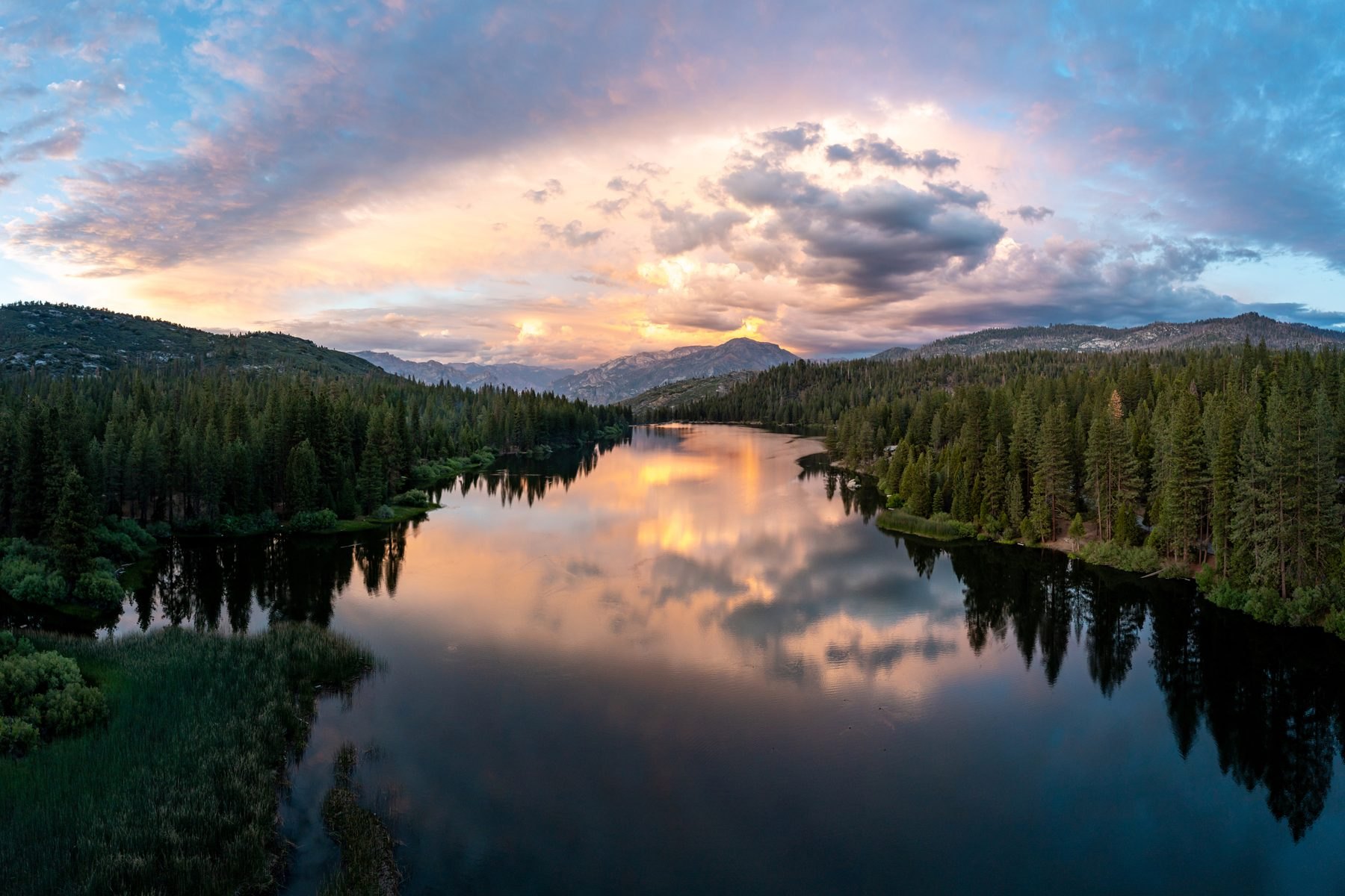 Sunset from the air over Hume Lake: still water holding pink and gold cloud, pine ridges on both shores and the Sierra Nevada beyond.