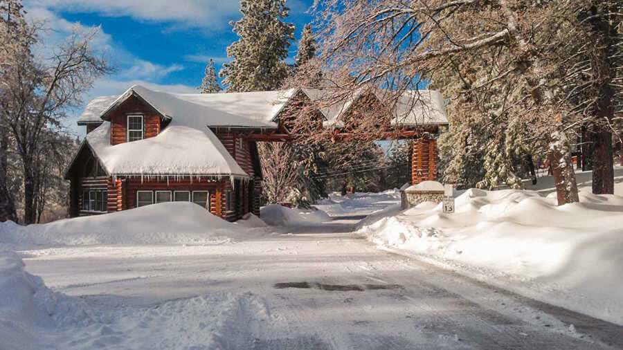 A log cabin at Hume SoCal under deep snow and a blue sky.