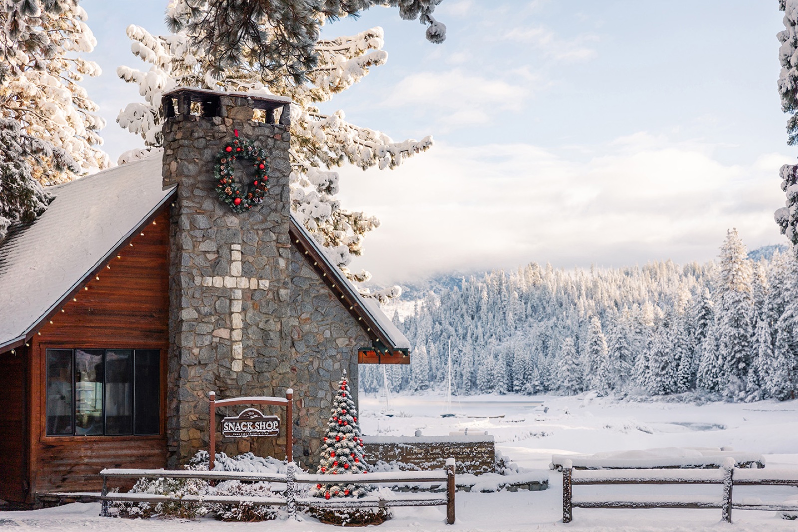 The snack shop at Hume Lake with a wreath and a lit Christmas tree, the frozen lake behind.