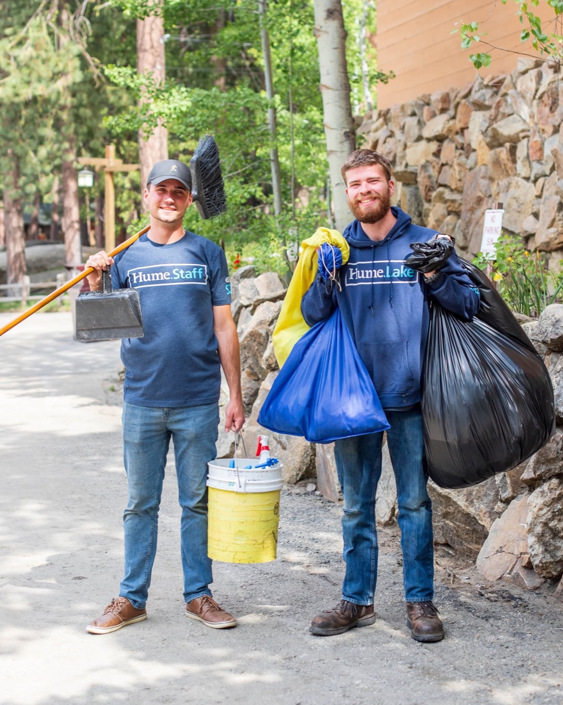 Two summer staff carrying trash bags and a bucket at camp.