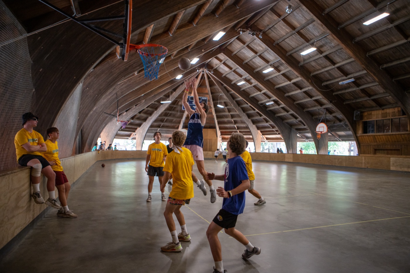 Campers playing basketball inside a timber-framed pavilion.