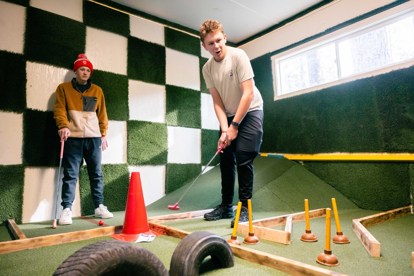 Two campers putting on an indoor mini golf hole.