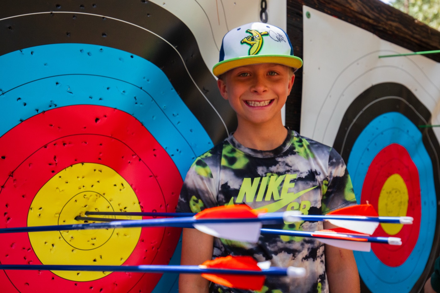 A camper grinning beside an archery target full of arrows.